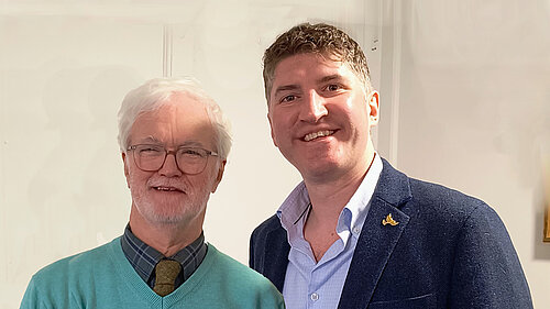 Robin Legg (Left) wearing a light blue jumper, grey checkered shirt and tie, and Edward Morello (right) wearing a navy blue suit jacket and light blue shirt