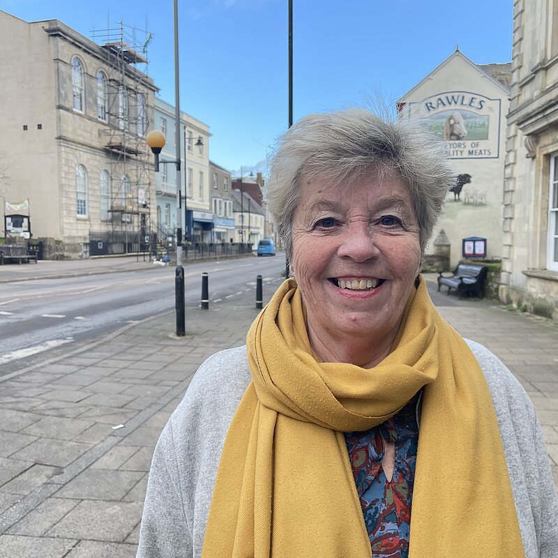 Bridget Bolwell in yellow scarf standing in Bridport.
