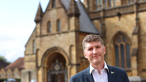Edeward Morello wearing a white shirt and blue suit jacket, outisde of Sherborne Abbey
