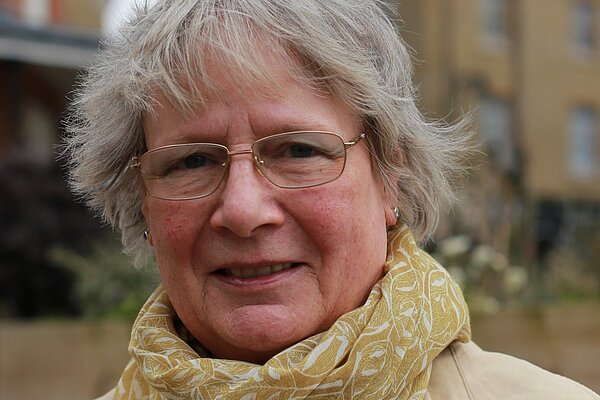 Frances Hogwood in 2019, wearing a beige trench coat and yellow scarf