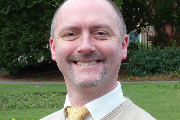 David Taylor wearing a tan sweater and a yellow tie.