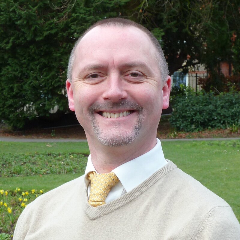 David Taylor wearing a tan sweater and a yellow tie.