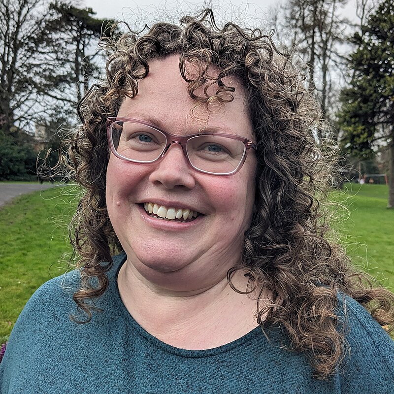 Vanessa Lloyd-Jones has curly hair and glasses and she is weraring a blue top