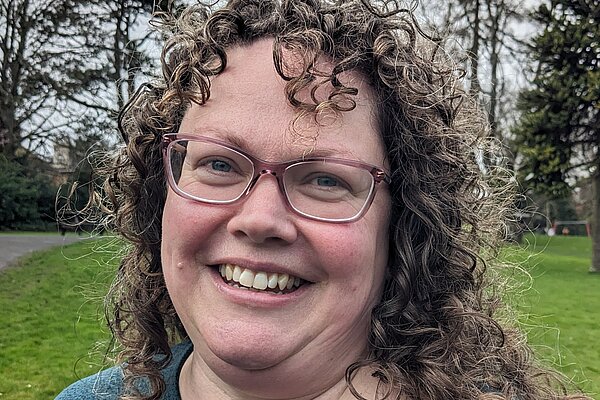 Vanessa Lloyd-Jones has curly hair and glasses and she is weraring a blue top