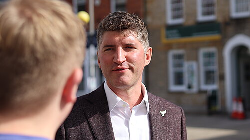Edward Morello talking to a young constistuent about his goals for West Dorset Edward Morello, wearing a white shirt and brown suit jacket, talking to a young constistuent in a blue t-shirt