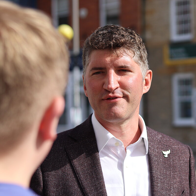 Edward Morello, wearing a white shirt and brown suit jacket, talking to a young constistuent in a blue t-shirt