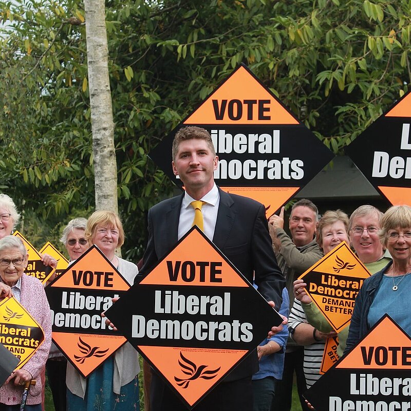 A group of activists with Edward Morello standing in the middle, all are holding Lib Dem orange placards 