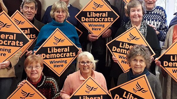A group of Lib Dem activists holding placards in a Village hall with Edward Morello