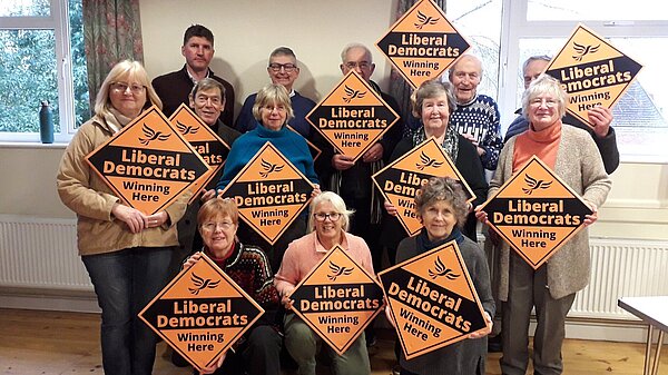 A group of Lib Dem activists holding placards in a Village hall with Edward Morello