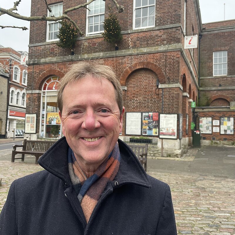 Nigel Rawlings stood outside of Bridport Town Hall wearing a black jacket and multicoloured scarf.