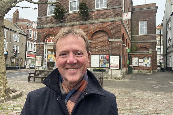 Nigel Rawlings stood outside of Bridport Town Hall wearing a black jacket and multicoloured scarf.