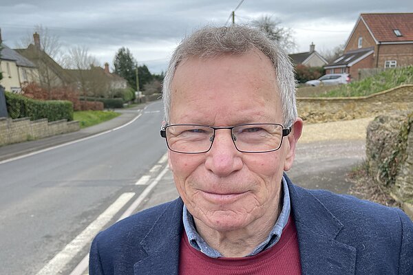 Chris Kippax wearing ared jumper and navy blue suit jacket in Longburton