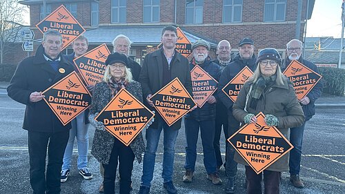 Parliamentary Candidate Edward Morello stood with Bridport Councillors in the Bridport Bus Station Car Park A Group of Lib Dem Activists holding Lib Dem Orange signs in Bridport Bus Station Car Park
