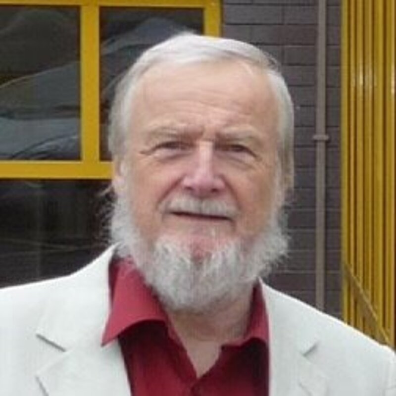 Dave Rickard is an older man with white hair and beard. In this image he is wearing a red shirt and white suit jacket